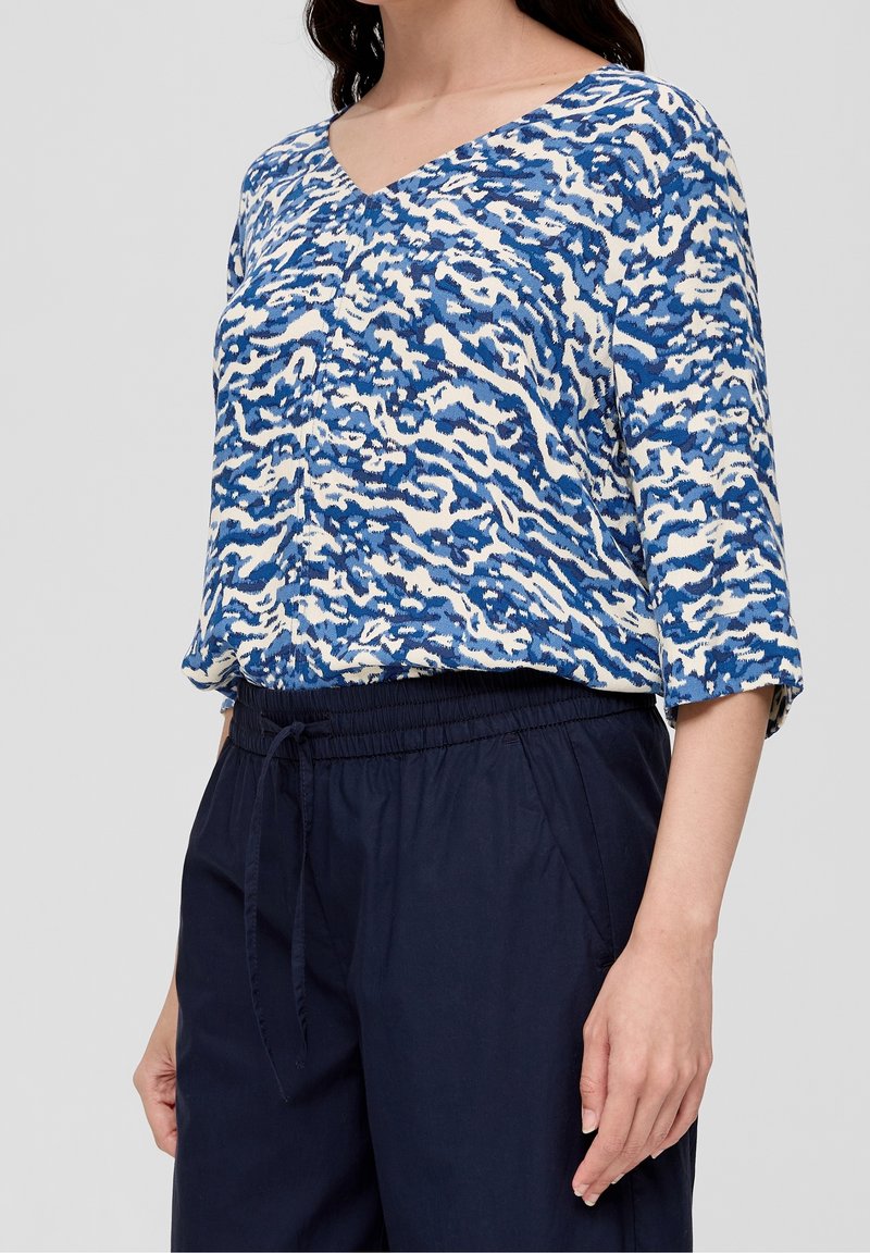 Top blu e bianco con motivo a fantasia, scollatura a V e maniche a tre quarti, abbinato a pantaloni navy con vita elastica. Tessuto morbido e strutturato.