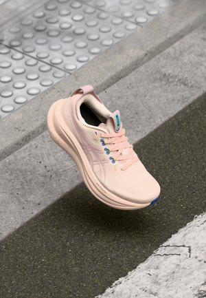 Light pink running shoe with textured upper, padded collar, blue accents, and reflective detailing. Features classic lace closure and logo.