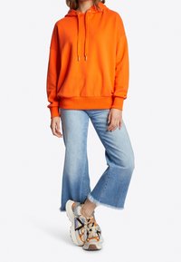 Pomarańczowy sweatshirt z kapturem, w luźnym kroju, z troczkami. W zestawie z jasnoniebieskimi, skróconymi, rozszerzającymi się dżinsami oraz wielokolorowymi, masywnymi trampkami.