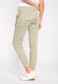 Ljusgröna cargobyxor med elastiska muddar, med sidofickor med dragkedja och bakfickor med klaff, kombinerade med vita sneakers.