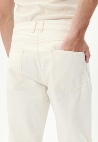 Jeans de denim de color claro con una textura suave, que cuentan con dos bolsillos traseros y una cinturilla ajustada, mostrados desde un ángulo trasero.
