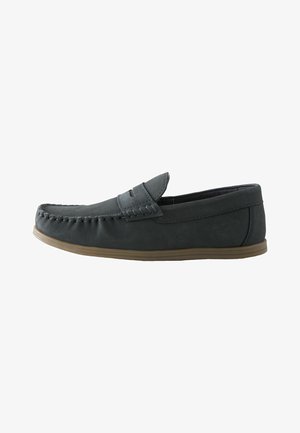 Mocassino slip-on in pelle nera con punta mocassino cucita e suola in gomma color cuoio, visto di lato su sfondo bianco.