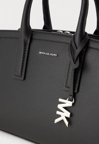 Svart skinnhandväska med dubbla topphandtag, strukturerad yta, silverfärgad logoplack och en silverfärgad "MK" charm som accent.