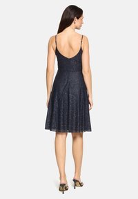 Robe bleu marine avec fines bretelles spaghetti, jupe évasée et texture scintillante. Dotée d'un dos plongeant et d'un ourlet arrivant au genou.