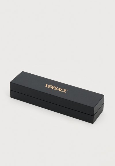 Boîte rectangulaire noire de marque Versace avec lettrage doré, fermée, posée sur une surface blanche.