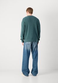 Groene, gestructureerde trui met een ontspannen pasvorm, gecombineerd met losse blauwe denim jeans met een vervaagd effect en klassieke achterzakken.