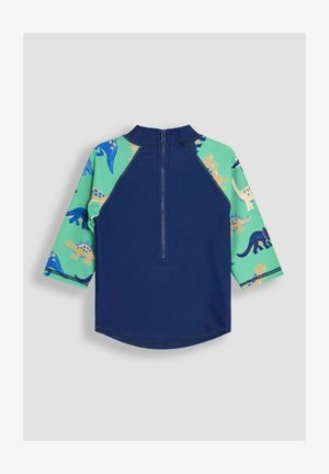Marineblauwe rash guard met lange mouwen en groene mouwen, versierd met kleurrijke dinosaurussen. Met ritssluiting aan de achterkant. Glad, rekbaar materiaal.