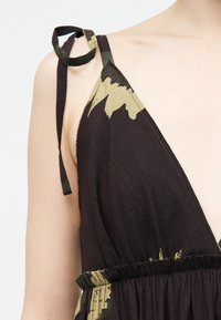 Κοντινό πλάνο καφέ και πράσινου αμάνικου φορέματος με κορδέλα στον ώμο που δένεται, πάνω σε γυμνό ώμο και άνω μέρος στήθους.