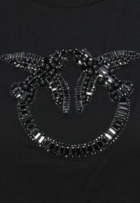Svart T-skjorte med et detaljert design som har store svarte perler og edelsteiner arrangert i et symmetrisk mønster som ligner vinger.