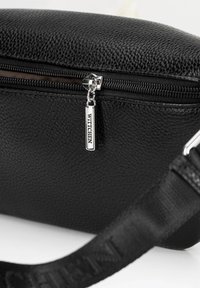 Černá texturovaná kabelka se zipovým uzávěrem, s stříbrným táhlem zipu a popruhem. Materiál se zdá být syntetický s zrnitým povrchem.