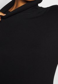 Czarny golf wykonany z prążkowanej dzianiny, z złożonym kołnierzem i dopasowanym krojem, podkreślający gładką teksturę i przylegający fason.