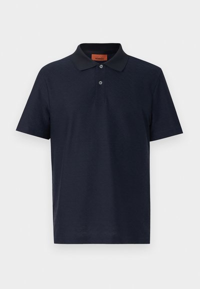 Μπλε ναυτικό μπλουζάκι πόλο με κοντά μανίκια, διακριτική υφή ζιγκ ζαγκ, ρεγκλάν με δύο κουμπιά και κλασικό γιακά, παρουσιασμένο σε απλό φόντο.
