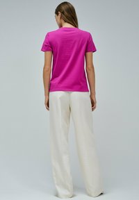 Camiseta ajustada de algodón rosa con mangas cortas, vista desde la parte de atrás. Combinada con pantalones de pierna ancha blancos sobre un fondo neutro.