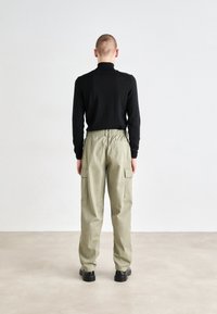 Top negro de manga larga, pantalones cargo caqui con cintura elástica y bolsillos laterales, combinados con zapatos negros de suela gruesa. Fondo neutro.