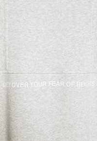 Felpa grigia chiara realizzata in tessuto morbido, con una trama liscia. Scritta "SUPERARE LA TUA PAURA DELLE ALTEZZE" stampata in bianco.