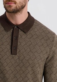 Braun gemustertes Polohemd mit strukturiertem Design, dunkelbraunem Kragen und drei Knöpfen am Ausschnitt, das eine gewebte Optik betont.
