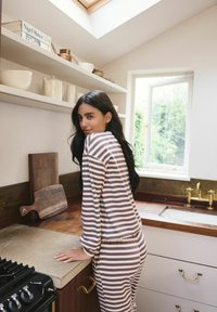 Striped loungewear in brown and cream, featuring relaxed fit. Modern kitchen setting with wooden shelves, brass faucet, and stone countertop.