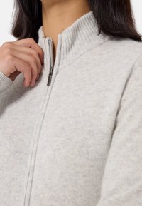 Maglione zip a grigio chiaro con colletto a coste, realizzato in tessuto morbido, caratterizzato da una texture liscia e da un delicato motivo melangiato.