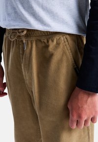 Lichtbruine corduroy broek met gestructureerde verticale strepen, voorzien van een elastische tailleband en een trekkoord voor verstelbaarheid.