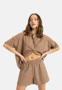 Kortärmad, cropped, skjortliknande överdel med knappar och matchande shorts i texturerat beige tyg med ett subtilt mönster och elastisk midja.