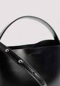 Schwarze Lederhandtasche mit einem geschwungenen Griff, sichtbar genäht und mit silbernen Hardware-Akzenten. Schlichtes, modernes Design.
