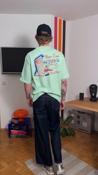 T-shirt oversize verde menta com um gráfico retro de motel nas costas, combinada com calças largas azul-escuro e sapatilhas brancas.