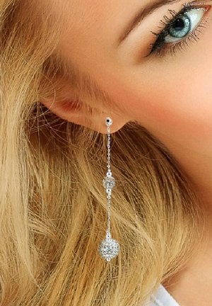 De élégantes boucles d'oreilles argentées à pendj ent, composées d'une chaîne avec deux sphères rondes et texturées, mettent en valeur leur design raffiné sur un fond de cheveux ondulés.