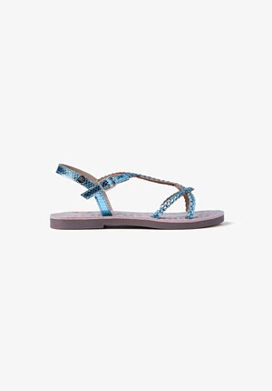 Sandalias planas metálicas azules con un diseño trenzado, con una correa de hebilla y una plantilla con patrón sobre una suela de color marrón claro.