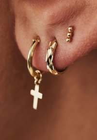 Gold hoop earrings featuring a smooth surface, a textured design, and a small cross pendant. A cluster of three gold stud accents also visible.