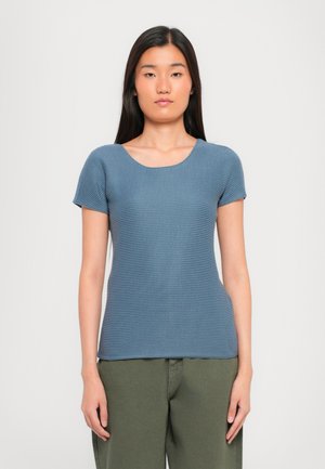 Maglietta a maniche corte, collo rotondo in tessuto blu texturizzato, silhouette aderente, con un leggero motivo a costine. Abbinata a pantaloni verde oliva.