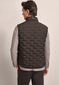 Dunkel gesteppte Weste aus gepolstertem synthetischem Material, mit hohem Kragen und glatter, matter Oberfläche. Graues Langarmshirt darunter.