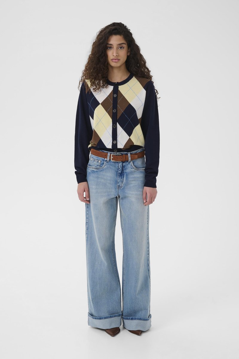 Cardigan marine avec motif argyle jaune, marron et blanc ; boutonné à l'avant. Jean large bleu clair avec ourlets retroussés et ceinture marron.