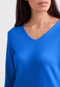 Maglione blu a collo a V con maniche lunghe, tessuto a coste e una vestibilità rilassata, che mette in risalto un tessuto liscio e morbido.