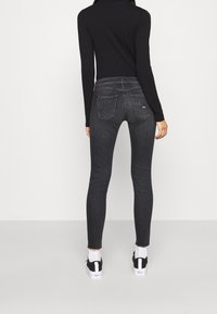 Suéter negro ajustado de cuello alto junto con jeans skinny gris oscuro que cuentan con dos bolsillos traseros y una cintura de media altura, combinados con unas zapatillas blancas y negras.