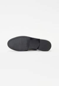Black leather shoe sole with a smooth texture, rounded toe, and stitched detailing along the edge. Flat heel with a slight curve.