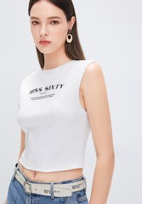 Biały, bezrękawnikowy crop top o prążkowanej teksturze z nadrukowanym logo "MISS SIXTY". Połączony z niebieskim dżinsowym paskiem z akcentami logo.