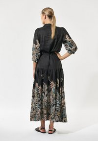 Sort linnedress med blomsterbroderi i pastelfarver, med et tætsiddende liv, puffærmer og et lagdelt skørt design.