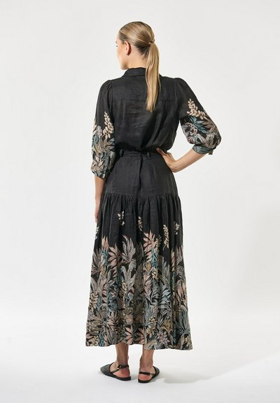 Robe en lin noire avec broderie florale aux couleurs pastel, présentant un corsage ajusté, des manches bouffantes et un design de jupe à volants.