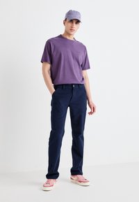 Purple cotton t-shirt, navy blue trousers, and pink sneakers. The cap is also purple, complementing the outfit's color palette.