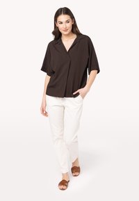 Camicia marrone a maniche corte con colletto, vestibilità comoda. Abbinata a pantaloni bianchi e sandali marroni con fasce. Tessuto liscio e design semplice.