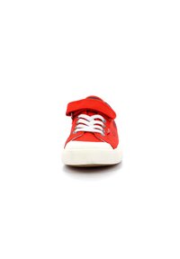 Zapatilla de lona roja con cordones blancos y correa ajustable. Cuenta con una suela de goma y una parte superior de textura suave. Diseño simple y deportivo.