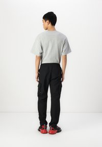 Grå t-shirt med korte ærmer, sorte cargo-bukser med sidelommer og røde og sorte sneakers. Enkel design med elastisk talje.