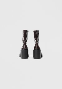 Bottines bordeaux brillantes à bout rond, avec une semelle compensée noire épaisse et une semelle texturée, présentant un design ajusté et une finition lisse.