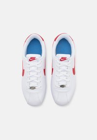 Balti sportiniai batai su raudonais akcentais, turintys lygią sintetinio paviršiaus medžiagą, mėlyną vidinę pamušalą ir baltas raišteles. Sidabrinis Nike logotipas ant liežuvėlio.