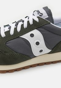 Green and gray athletic shoe featuring suede and fabric materials, with white logo accents, round holes, and a beige rubber sole.