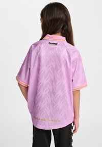 Lila kortärmad tröja med geometriskt mönster, gul och rosa kant, samt "INTERNATIONALS" i guld på ryggen. Material: lättviktigt tyg.