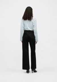 Μπλούζα με μακρύ μανίκι σε ρίγες σε ανοιχτό μπλε και λευκό, συνδυασμένη με ψηλόμεσα μαύρα φαρδιά τζιν παντελόνια, προβαλλόμενη από πίσω.