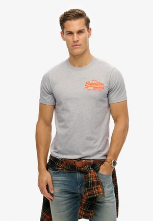 Gray cotton t-shirt with short sleeves and a crew neck, featuring an orange "SuperDry" logo on the chest. Textured plaid shirt tied around waist.