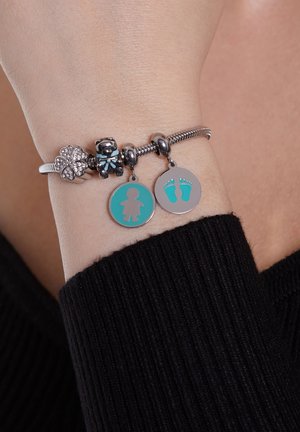 Zilveren charmearmband met teal accenten, waaronder een beer, een bloem met rhinestones, en twee ronde pendanten met een figuur en voetafdrukken.