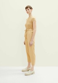 Helles goldenfarbenes Kurzarmoberteil, kombiniert mit hochgeschnittenen, taillierten Hosen und cremefarbenen Plateauschuhen. Glatte Textur, einfaches Design, flexibler Sitz.